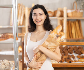 Young woman buyer chooses tasty fresh baguettes in bakery