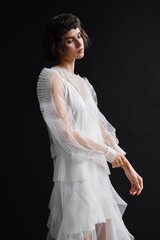 Elegant model poses in sheer layered dress against a dark background in a fashion studio setting