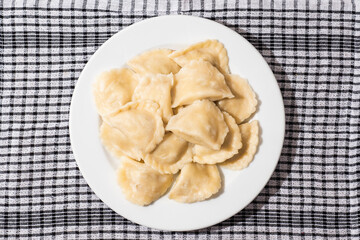 A plate of dumplings sits on a checkered cloth. The dumplings are white and arranged in a neat pile, Popular East European food. Simple easy meal.
