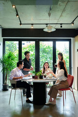 Asian Adult Professionals Enjoying Lunch Break Together in Modern Office Space Discussing Business Strategies and Building Teamwork in Friendly Environment