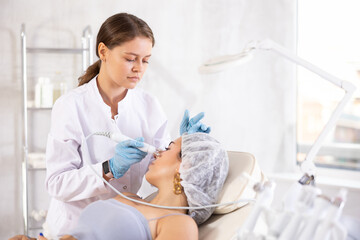 Young brunette girl having facial beauty massage with beauty machine attachment making by European...