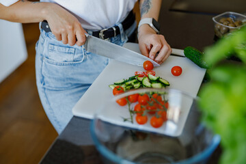 A person chopping vibrant cherry tomatoes and fresh cucumber on a cutting board, preparing healthy meals