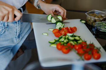 A closeup view showcasing fresh tomatoes and crisp cucumbers as they are being chopped on a wooden cutting board