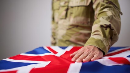 British soldier in uniform placing hand on UK flag, Remembrance Day tribute, honoring fallen heroes, military respect, national commemoration
