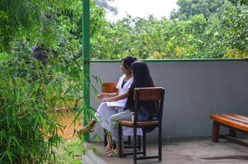 Fototapeta premium A lighthearted chat and warm smiles are exchanged by two teen girls while sitting under a shelter during the rain in a tranquil park.