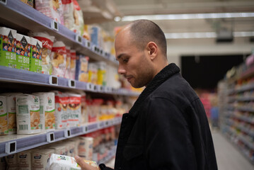Man holding two different food products while deciding which one to buy. Reflects comparison shopping, healthy lifestyle, and mindful consumer habits.