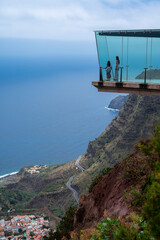 A couple is standing on a glass bridge looking out over the ocean. The view is breathtaking and the couple is enjoying the moment
