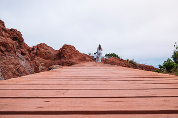 A woman and a child are walking on a wooden bridge over a rocky hill. The bridge is narrow and the woman is holding the child's hand. Scene is peaceful and serene, as the woman