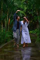Two teenage girls laugh and joke while walking on a garden path soaked by recent rain, enjoying the...