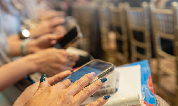People sitting in a conference or seminar setting, actively using their smartphones. Hands with devices, reflecting modern engagement and digital interaction. - Powered by Adobe