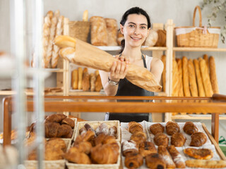 Young woman seller holding basket with fresh croissants in bakery