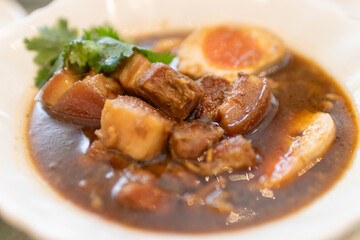 Delicious bowl of savory pork stew with eggs and fresh herbs garnishing.