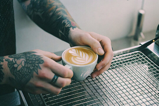 tattooed barista serving latte coffee