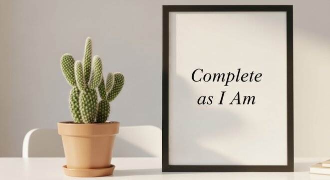 small potted cactus on a white desk next to a framed quote: "Complete as I Am." - Powered by Adobe