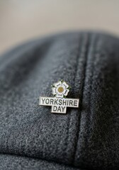 Yorkshire Day enamel pin with white rose emblem attached to traditional flat cap. Symbol of regional pride in Northern England