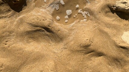 Golden sand ripples with frothy remnants, invoking Desert Bathing Day and Sand-Sifting Festival,...