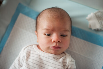 Cute baby lies comfortably on a soft, quilted surface. The infant wears a striped outfit, exuding...