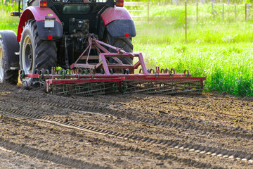 Tractor tilling soil in sunny field with greenery and freshly plowed earth