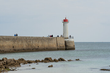 A scenic coastal view with a white lighthouse at the end of a stone pier