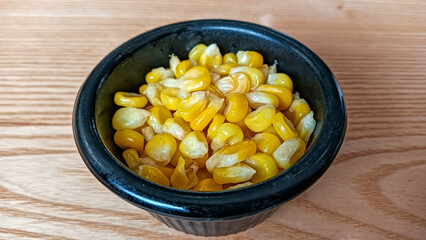 A close-up of a black bowl filled with vibrant, juicy sweet corn kernels, served fresh and ready to eat.