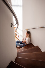 Young mother breastfeeding her newborn baby while sitting comfortably on wooden stairs at home, savoring the joys of motherhood and nurturing moments filled with love and care