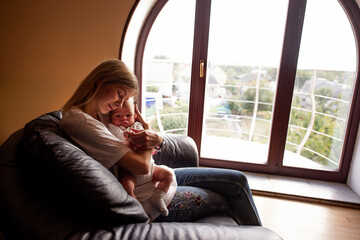 Serene moment captured as a mother lovingly holds her baby on a cozy leather sofa, with soft natural light streaming through a large arched window, creating a peaceful atmosphere