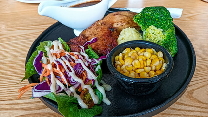 A complete Western-style meal featuring grilled chicken chop served with mashed potato, broccoli, sweet corn, salad, and rich brown sauce on a black plate.