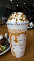 A refreshing caramel frappe topped with whipped cream and crunchy granola, served in a plastic cup with a dome lid.