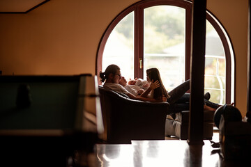 Parents and children are cuddling on a comfortable armchair near a window, enjoying a quiet moment of togetherness and creating a warm family atmosphere