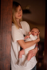 Young mother gently cradles her newborn baby in a warm, cozy home setting. The intimate moment captures the bond and tenderness between mother and child, highlighting early parenthood