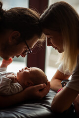 Tender moment as parents lovingly cradle their newborn, creating a warm and intimate family bond. Soft light highlights the emotional connection and nurturing atmosphere