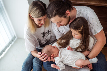 Joyful family gathers around their newborn baby, expressing love and warmth. Parents and sibling share a tender moment, highlighting family bonds and new beginnings in a cozy home setting