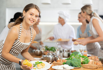Girl visiting culinary school completes preparation of tender dietary poultry meat and puts small amount of spicy sauce on fillet