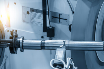 The operation of cylindrical surface grinding machine with the metal shaft parts in the light blue scene.