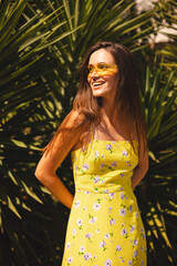 Brunette long hair woman standing near palm tree and look coquette back, flirty smiling. Woman wear...
