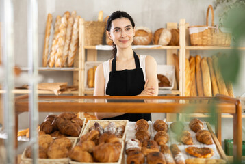 Armenian with long hair work in sales area of small cozy store, family bakery. Entrepreneurs present their goods in showcase, demonstrate sweet pastries and croissants.