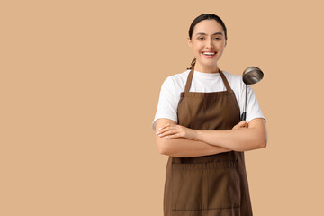Young woman in apron with ladle on beige background