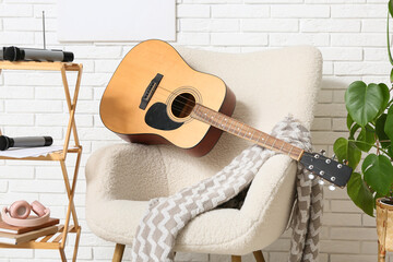 Modern acoustic guitar on white armchair in stylish living room