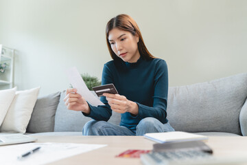 young woman looking at credit card invoice checking receipt before pay debt via mobile app at home