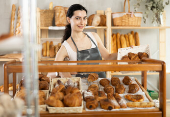 Authors bakery, family business idea. Young female sales consultant puts croissants on counter, complements assortment with fresh rolls, puts ready-made croissants in glass case