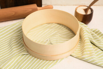 Wooden sieve, napkin, bowl of flour, rolling pin on light table