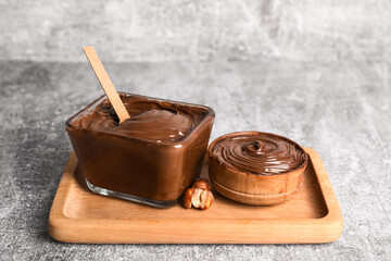 Bowls of sweet chocolate spread and hazelnuts on grey background