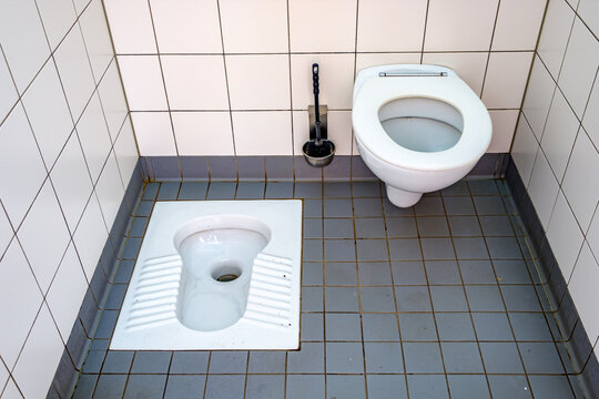 Unique restroom setup featuring a standard toilet and a squat toilet in a tiled space during daytime