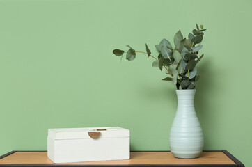 Box and vase with eucalyptus branches near green wall in room, closeup