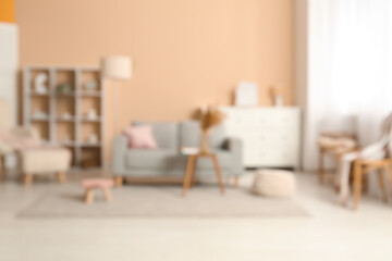 Blurred view of living room with comfortable sofa, pouf and table near beige wall
