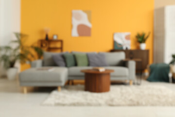 Blurred view of living room with comfortable sofa and table near yellow wall