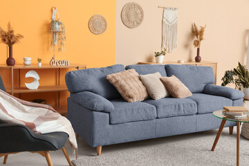 Comfortable grey sofa near color wall in interior of living room, closeup