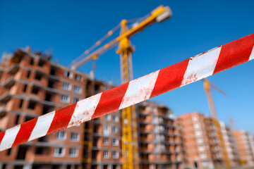 Red and white caution tape blocking access to construction site with cranes and building