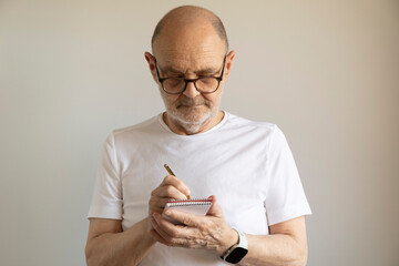 Senior Man Writing Notes in a Notebook While Reflecting Thoughtfully