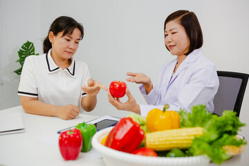 An Asian female nutritionist attentively discusses dietary habits with a patient, offering...
